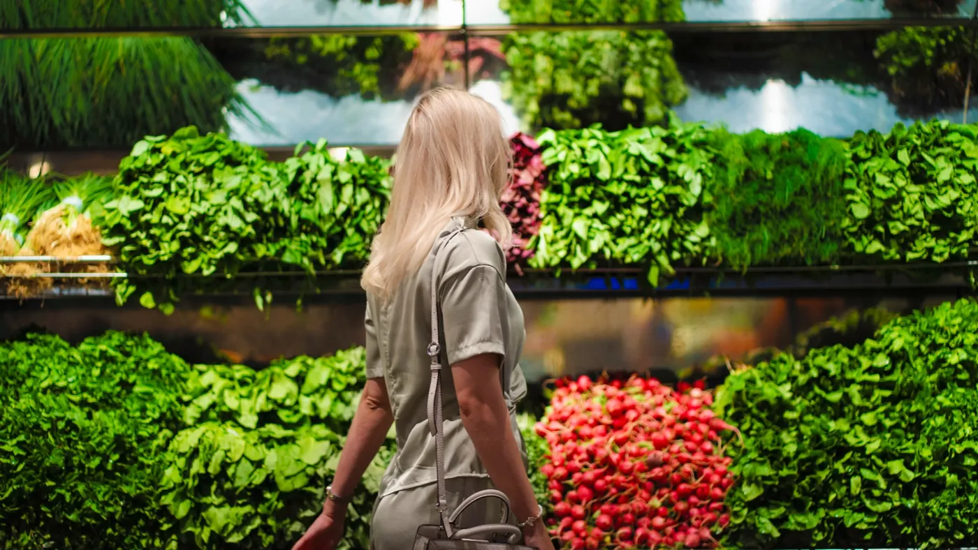 A woman choosing fresh greens and vegetables at a produce market.